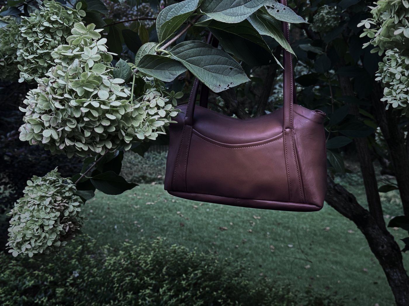 The Oxbo Shoulder hanging by its straps, hydrangeas behind it at dusk