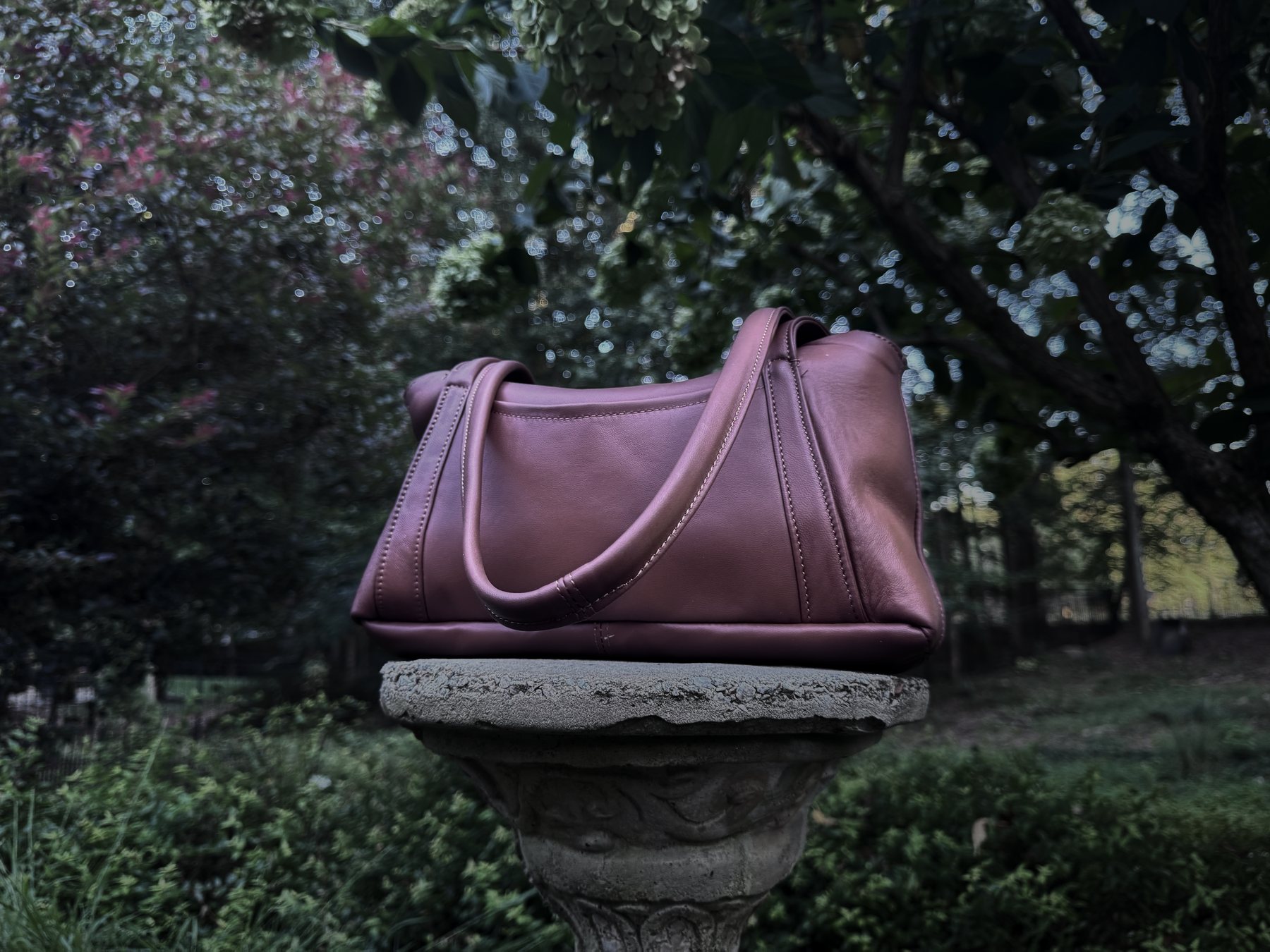 The Oxbo Shoulder in damson lambskin on a stone plinth, lit from the left